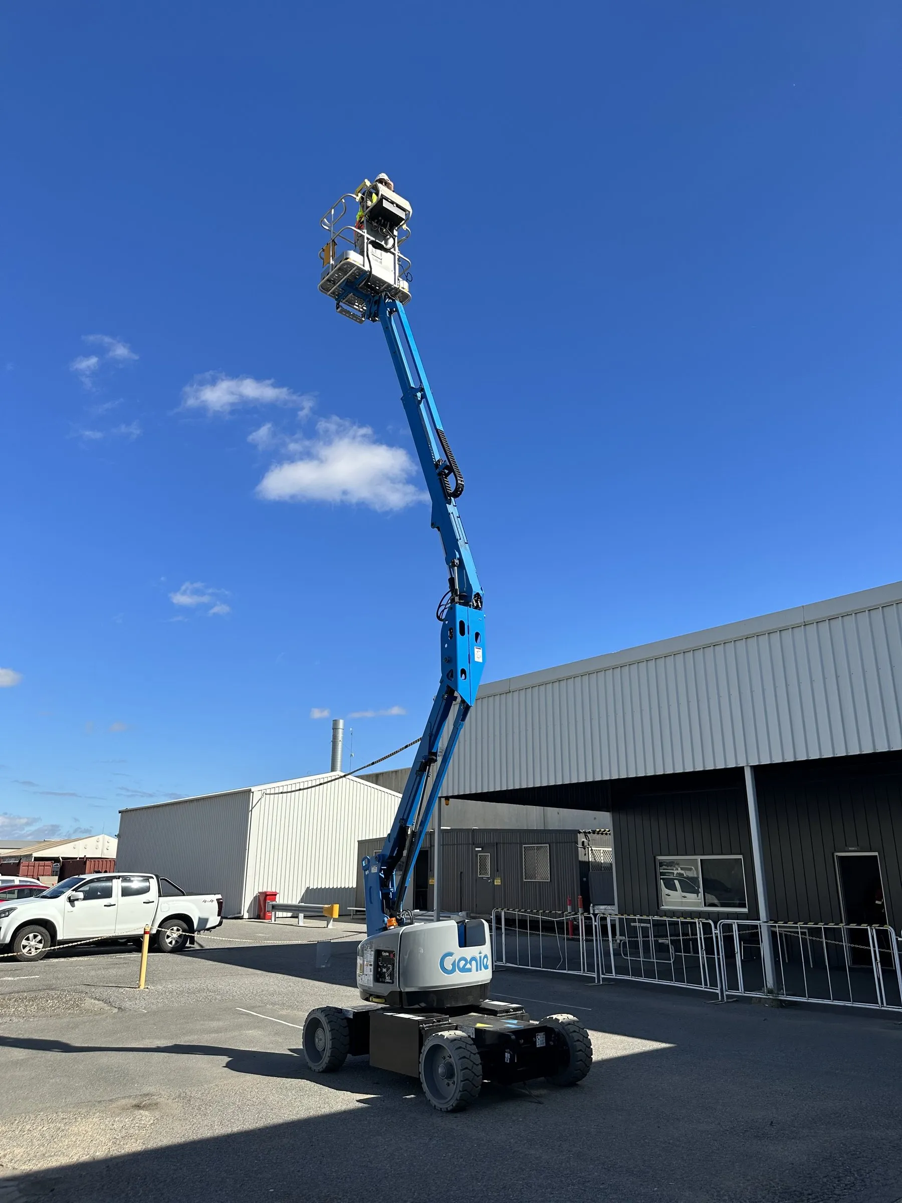 Blue boom lift raised beside a warehouse under a blue sky