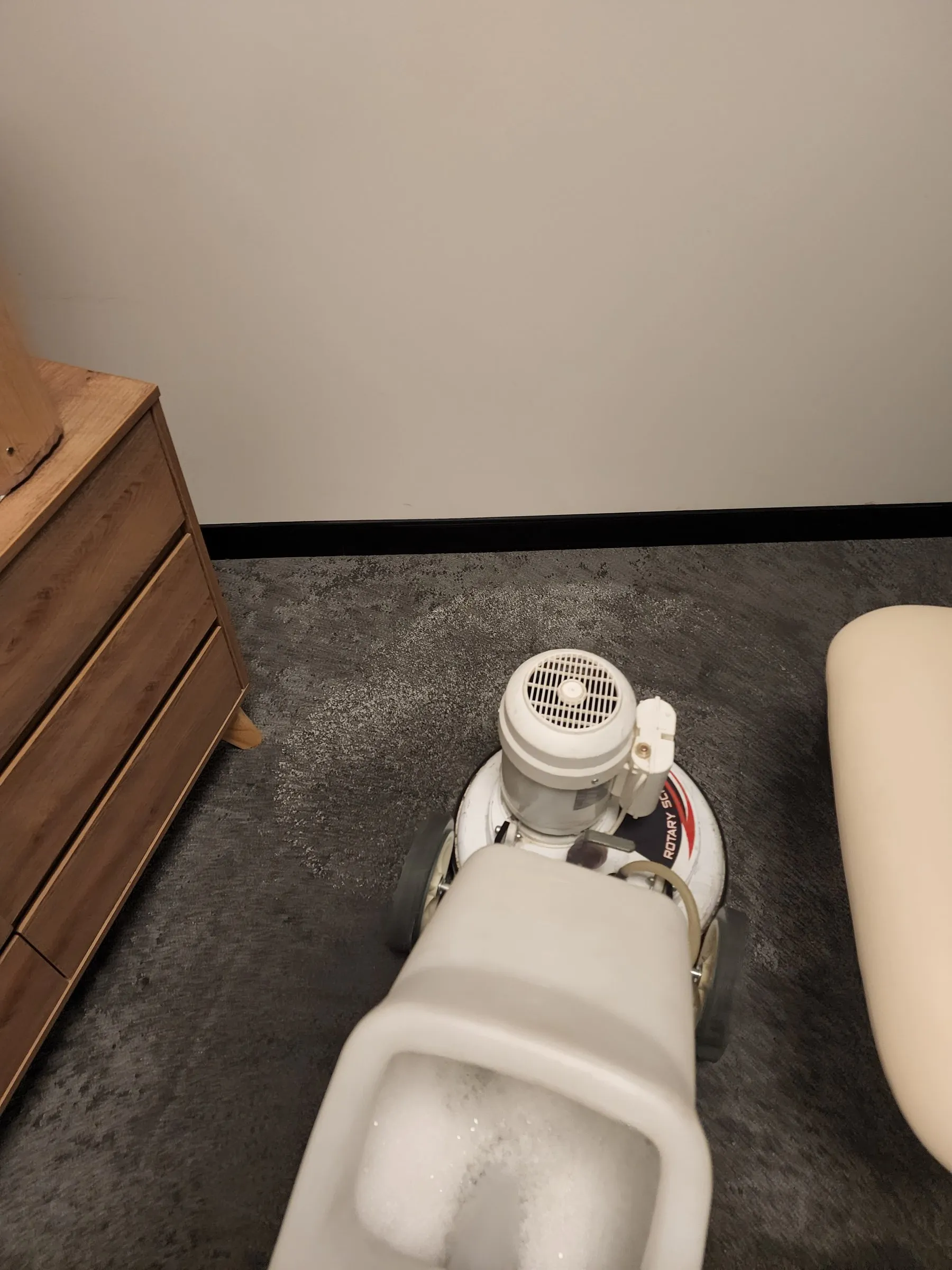 Rotary machine cleaning dark carpet beside timber furniture