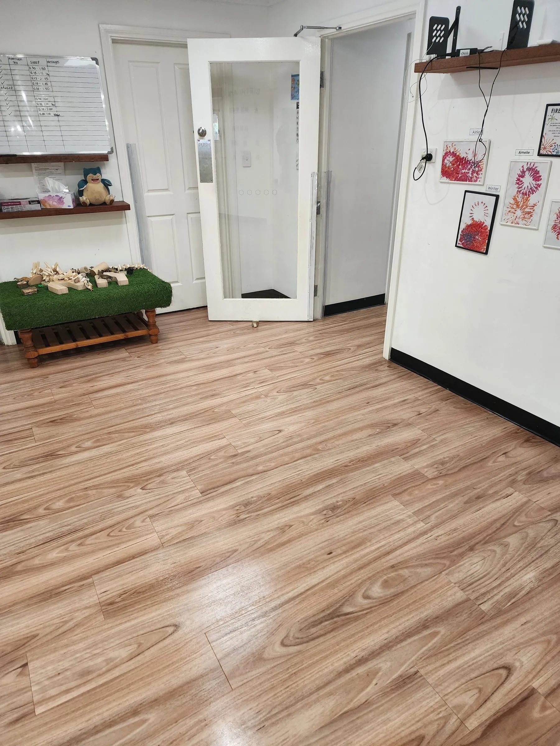 Bright childcare room with a timber-look floor and children's shelving