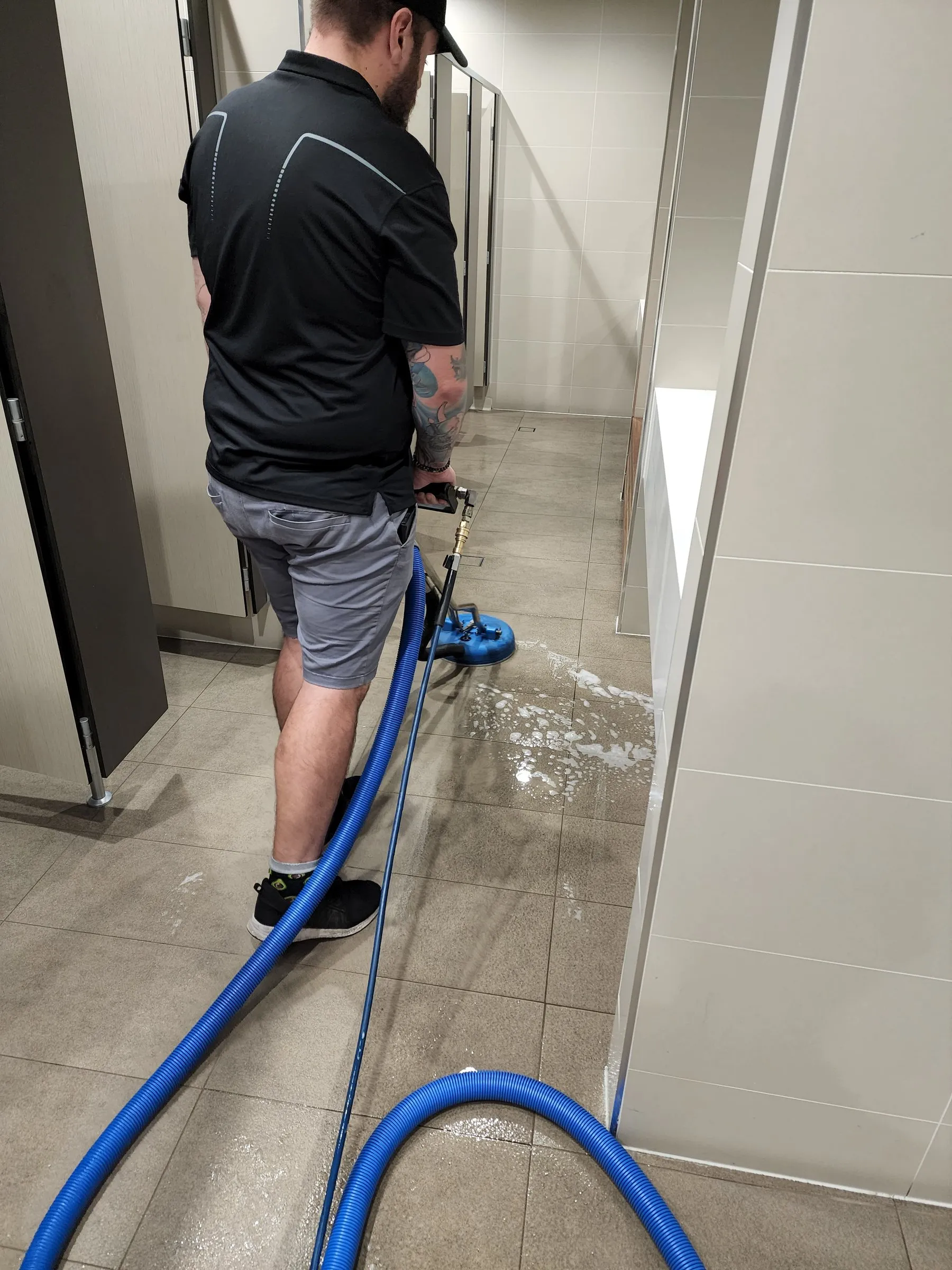 Technician with a hose scrubbing a long tiled corridor