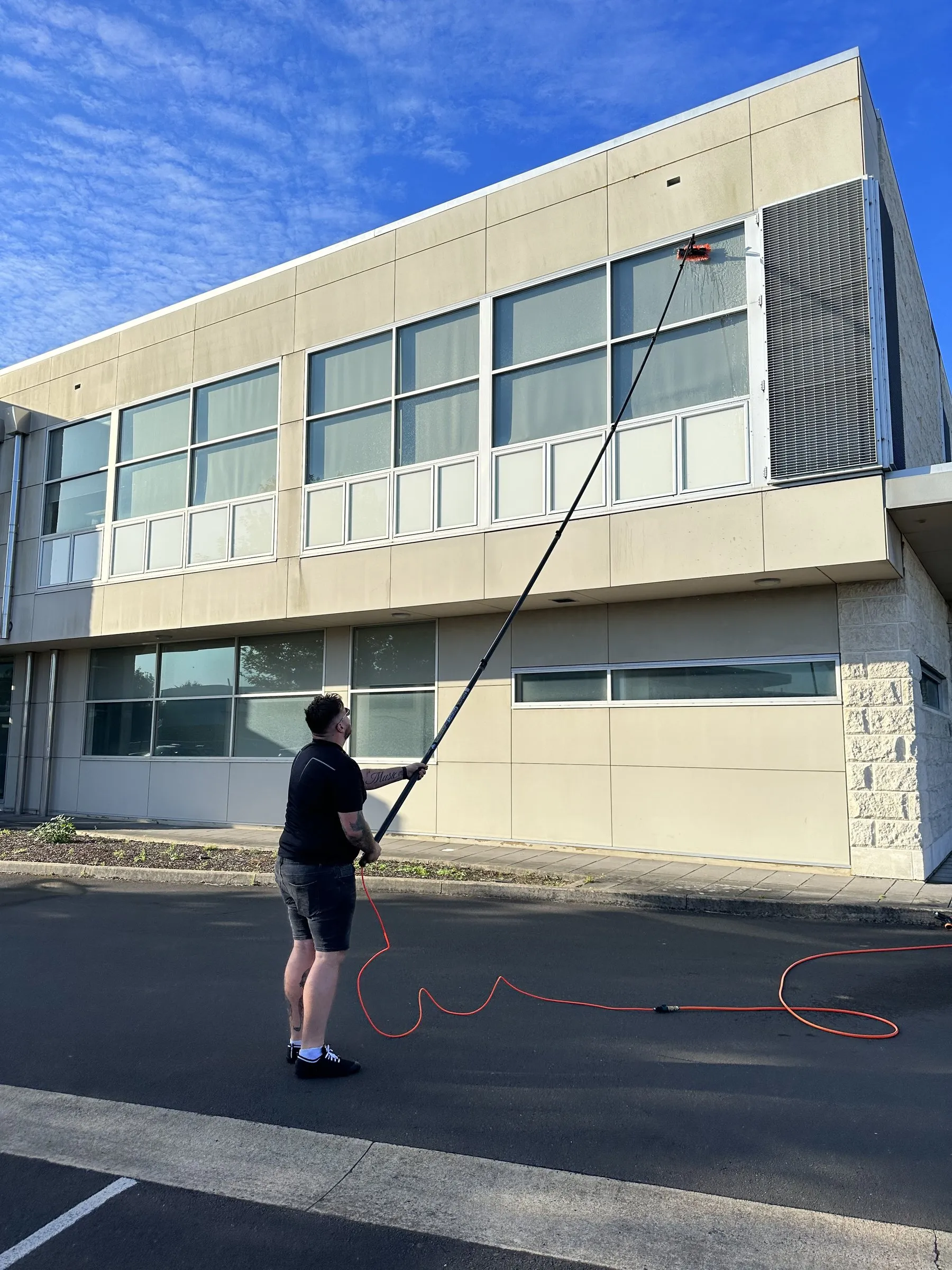 Technician with a water-fed pole cleaning first-floor windows on a cream building