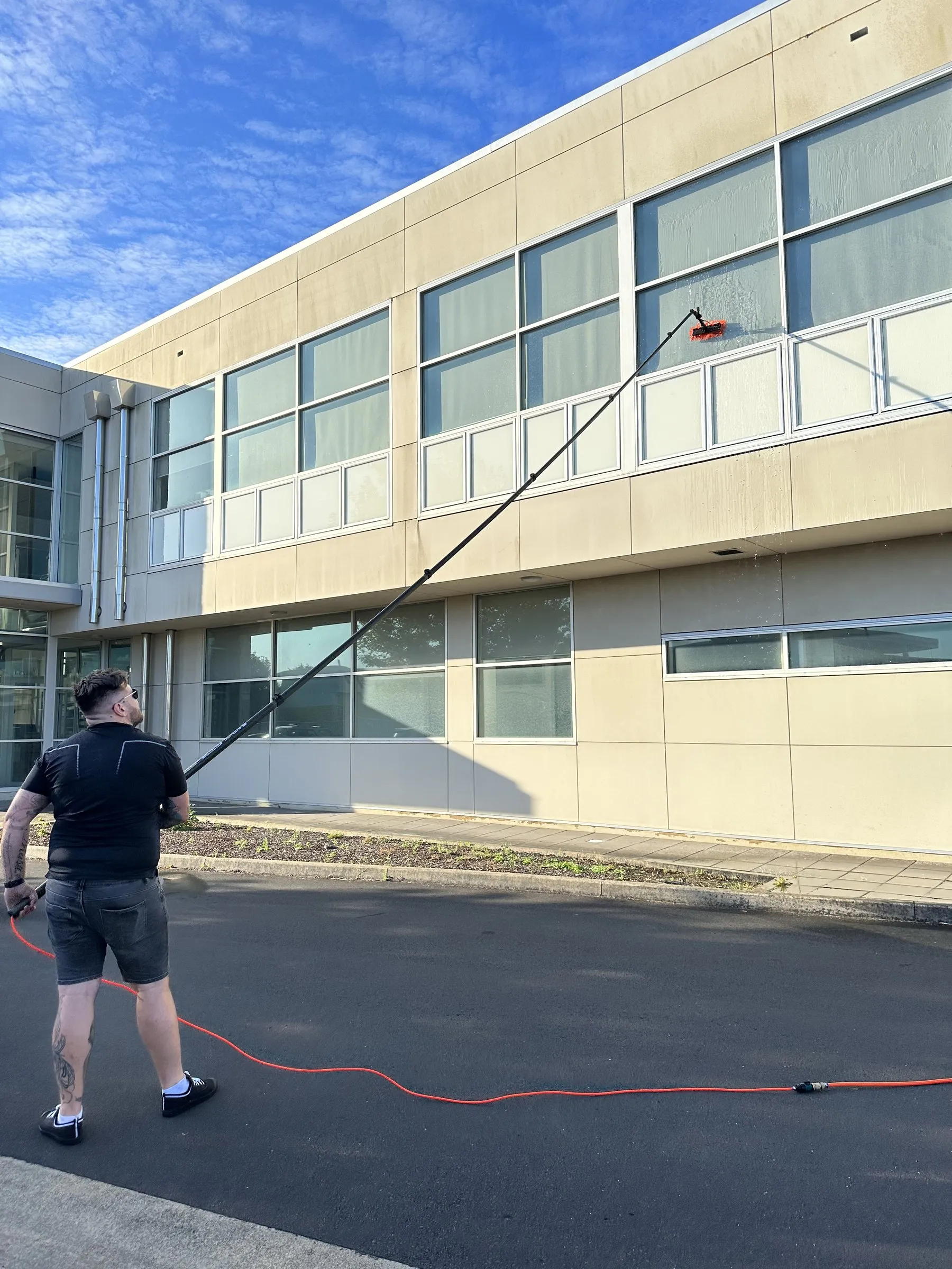 Technician using a water-fed pole on first-floor windows of a cream two-storey building