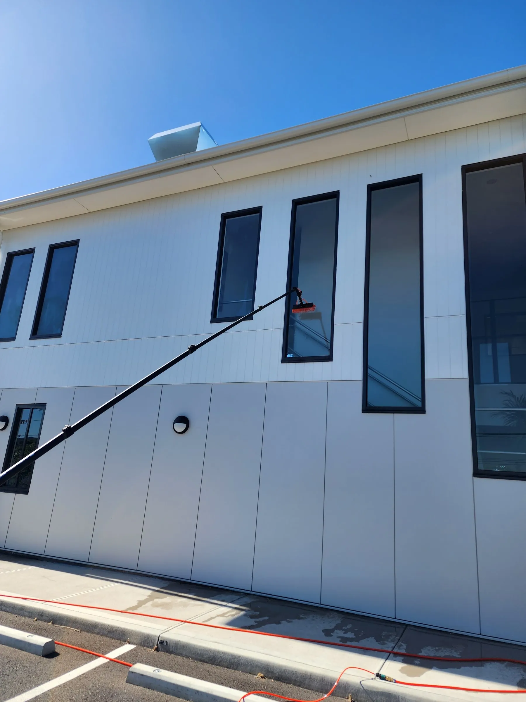 Water-fed pole cleaning the windows of a modern white building