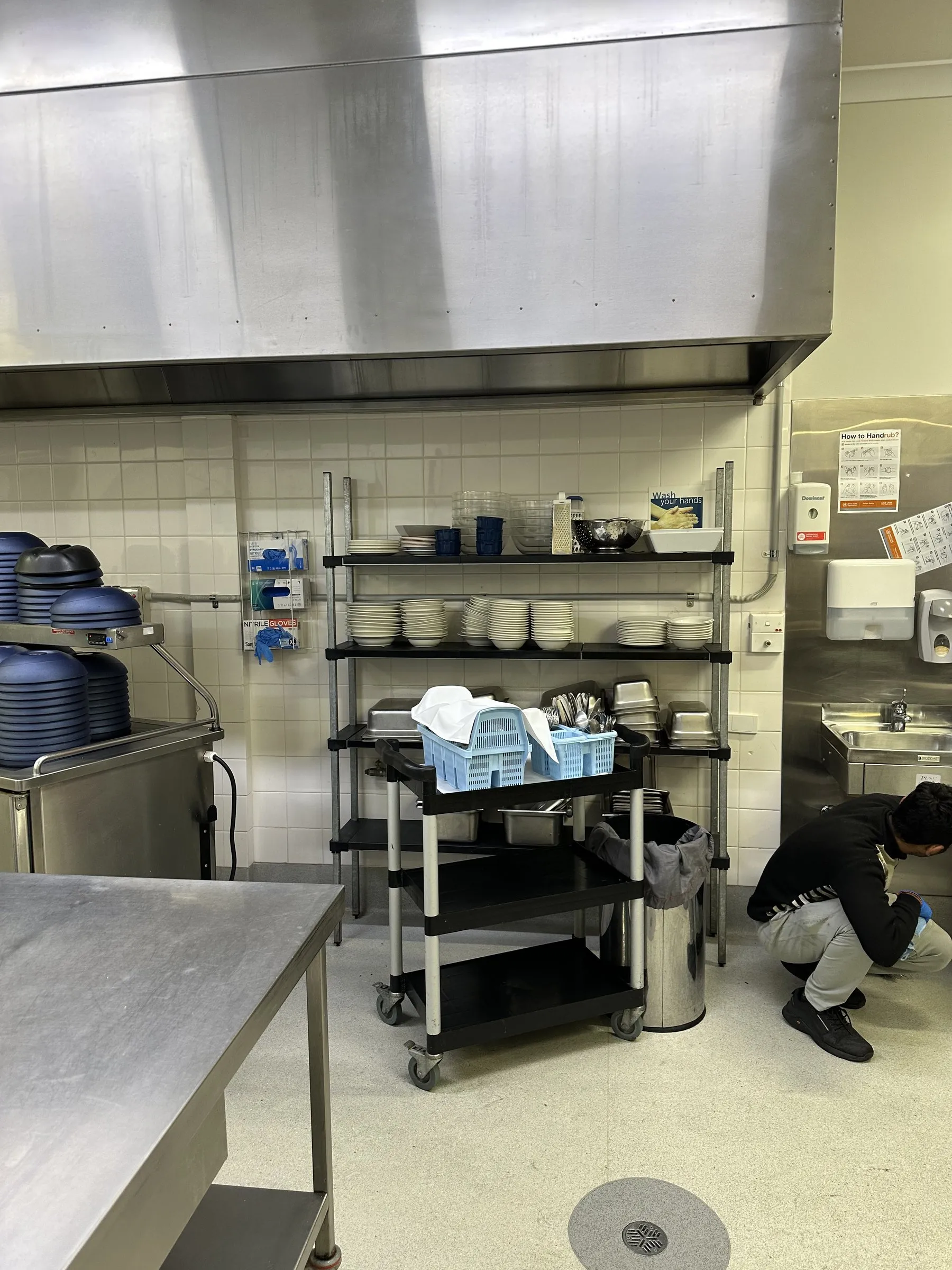 Commercial kitchen deep clean, one person cleaning under a stainless bench