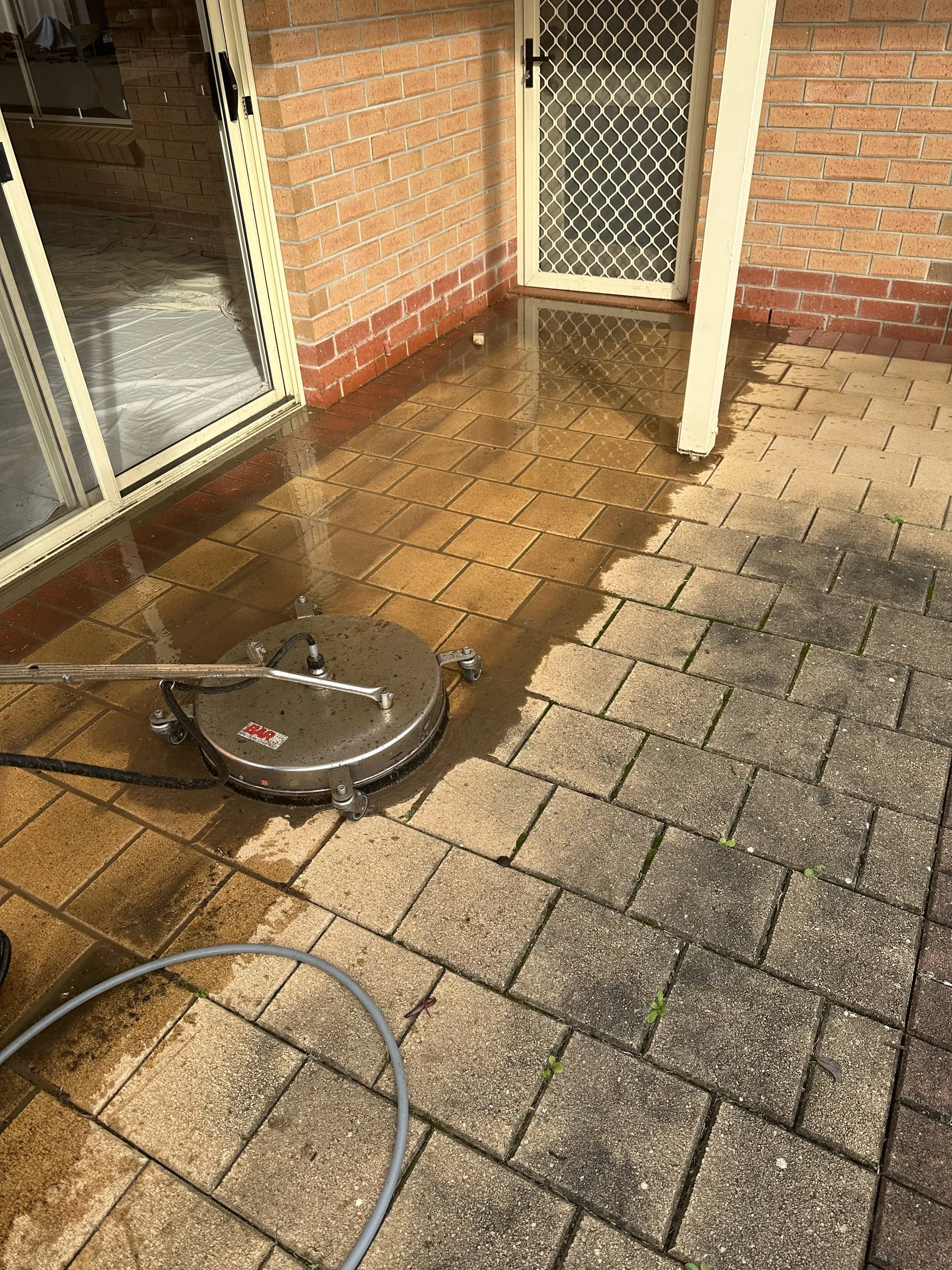 Surface cleaner on brown pavers, half done, with a clear clean line