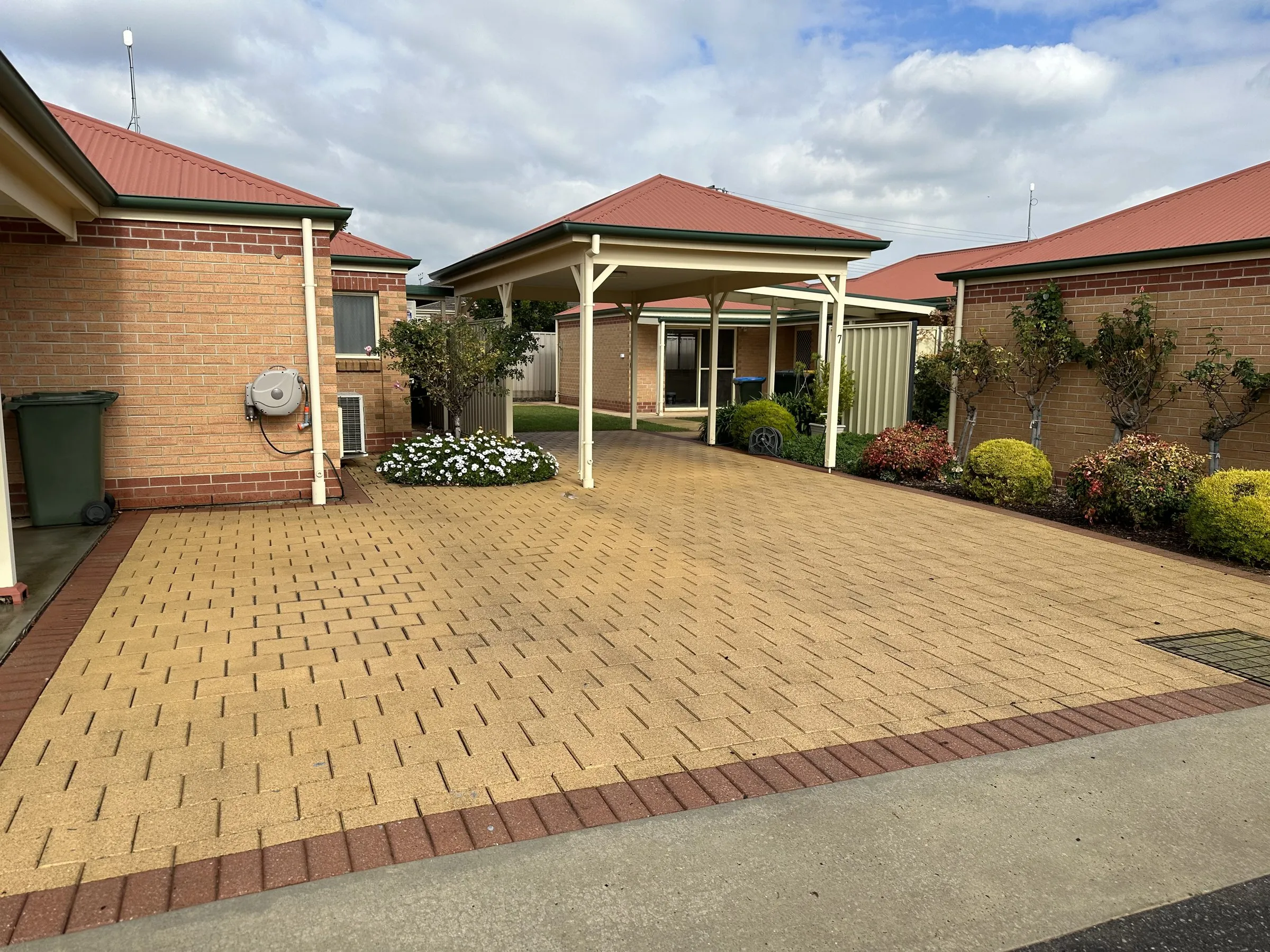 Unit courtyard with brick pavers, a pergola and bins