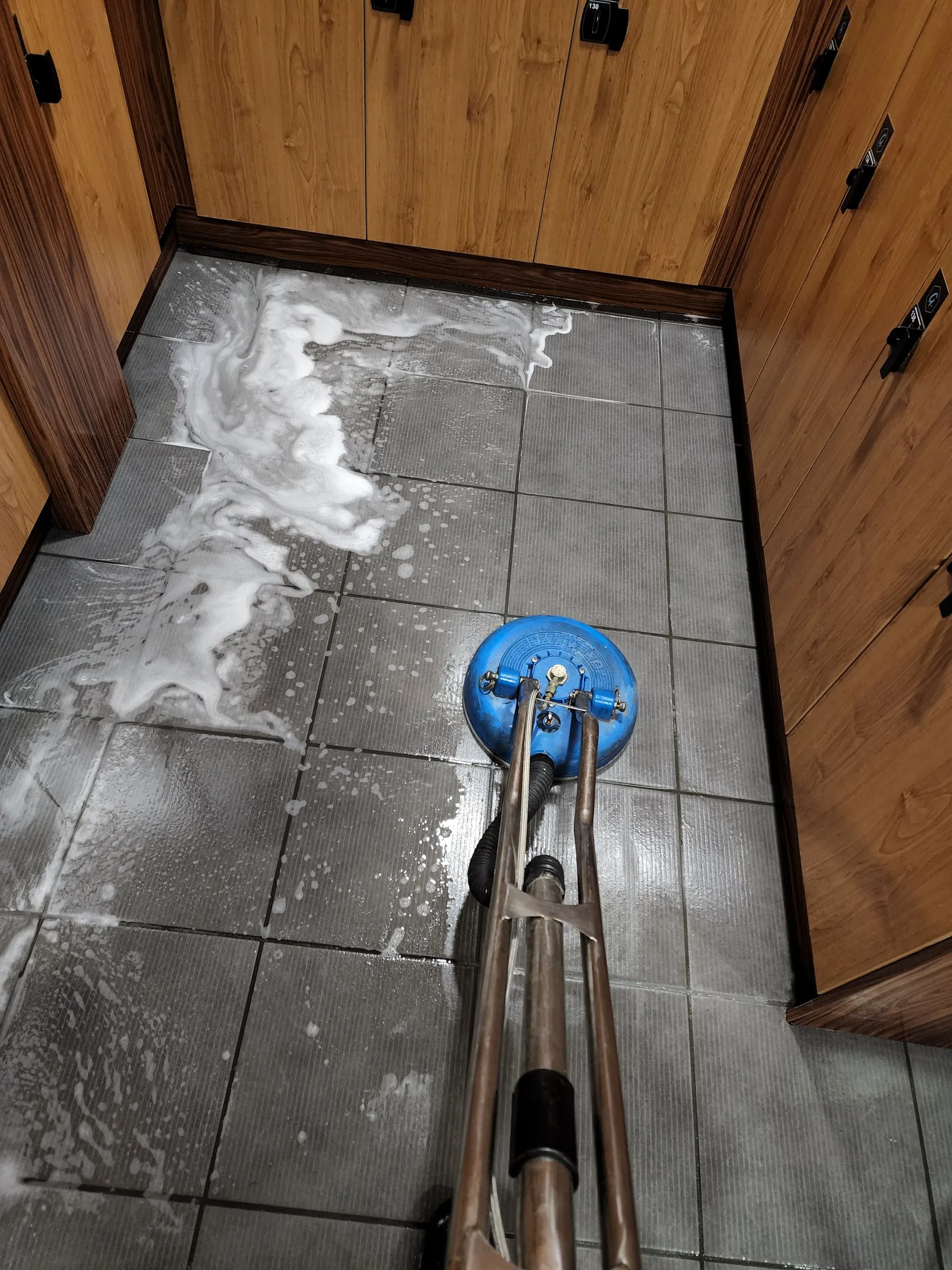 Spinner wand scrubbing a tiled change room floor beside timber lockers