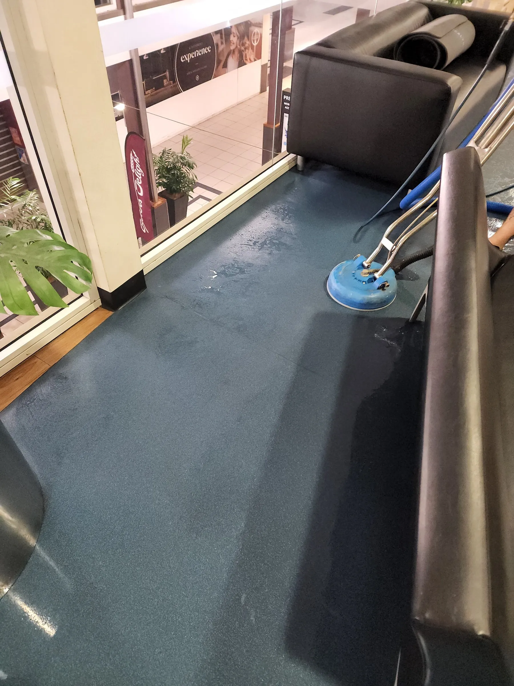 Spinner wand scrubbing blue vinyl flooring beside a lounge