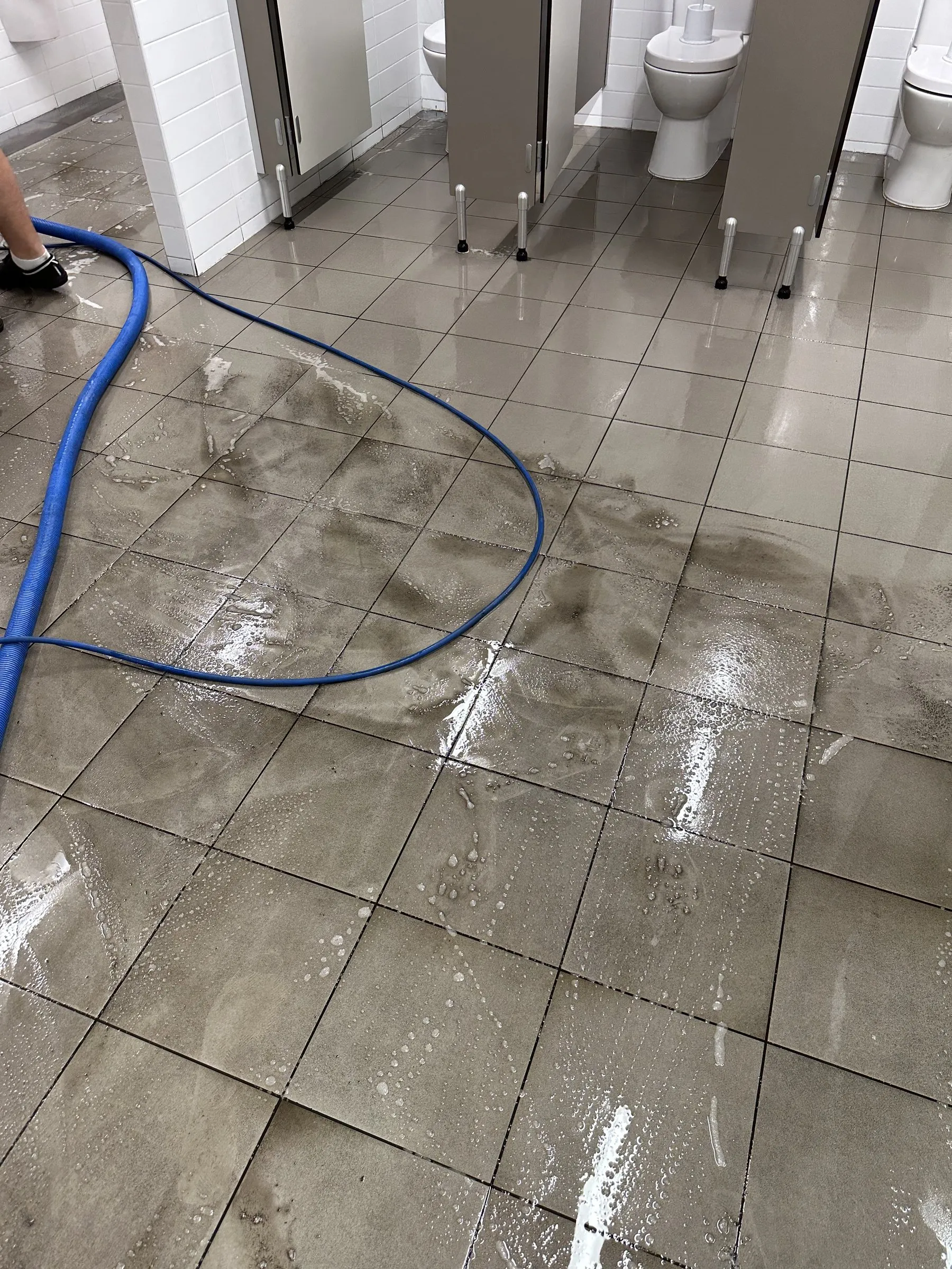 Washroom floor mid-clean with a hose on grimy grout