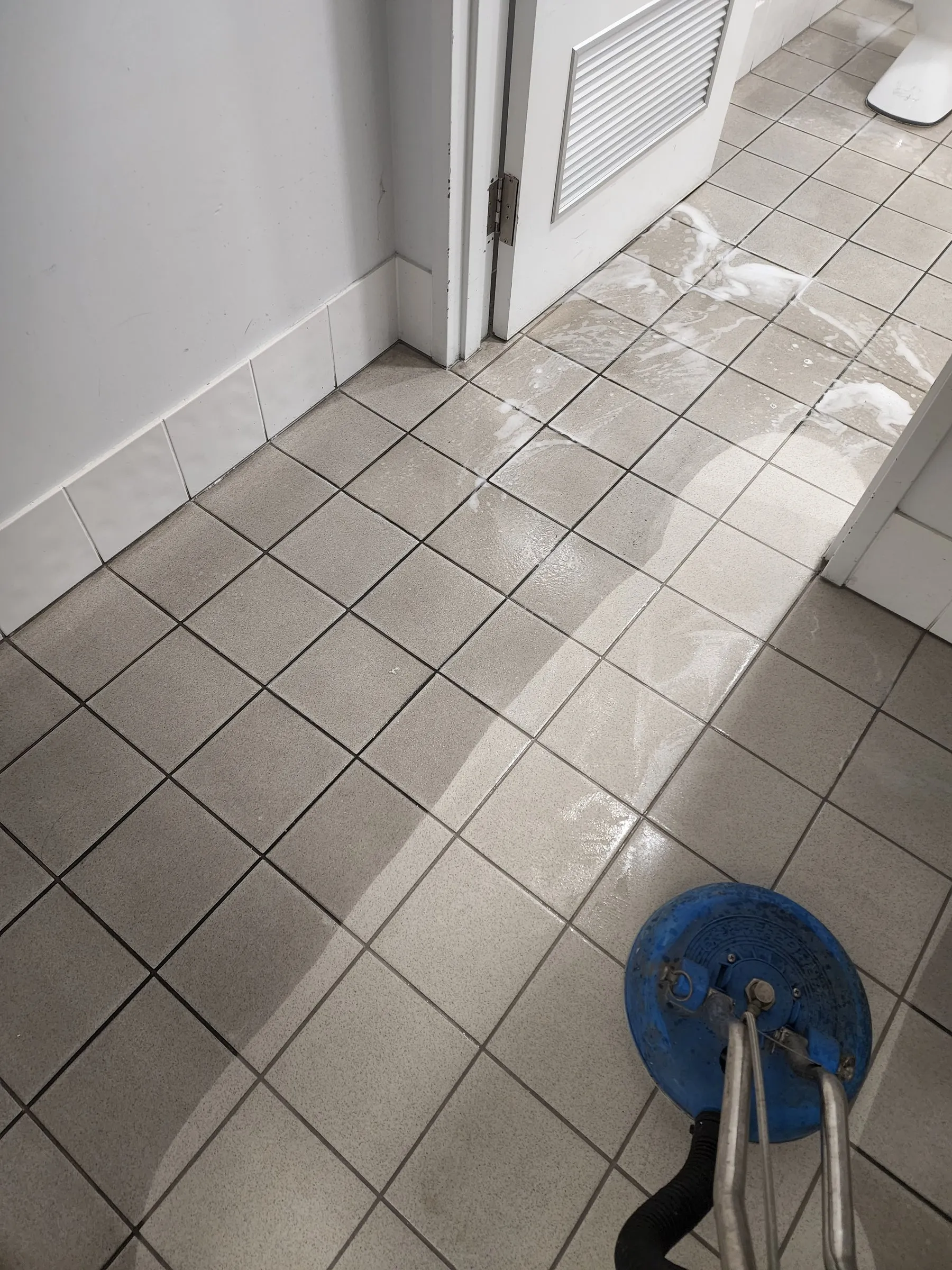 Spinner wand scrubbing white square tiles in a corridor